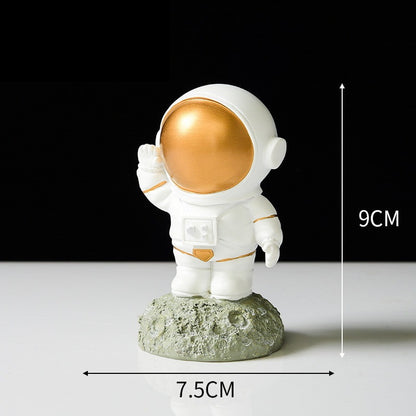 Ornament's style O is an astronaut wearing a gold visor standing on a stone holding hand.