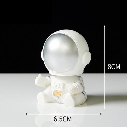 Ornament's style Q is an astronaut wearing a silver visor sitting on the ground with his hands slightly open.