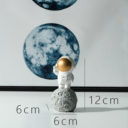 Ornament's style H is an astronaut wearing a gold visor standing on a round stone holding hand.