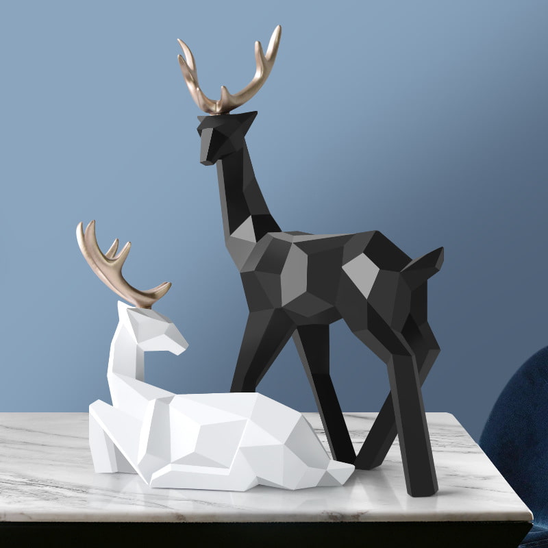 Two geometric deer sculptures, one standing in black and another sitting in white, displayed on a table.