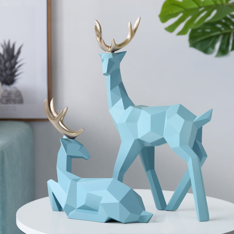 Two geometric deer sculptures in blue, one standing and another sitting, displayed on a table.