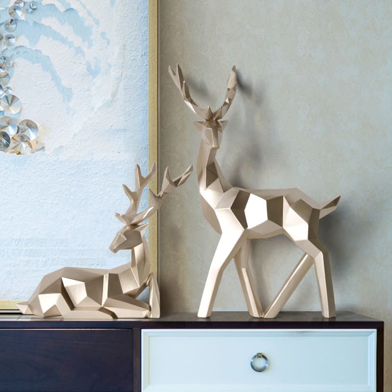 Two geometric deer sculptures in gold, one standing and another sitting, displayed on a table.