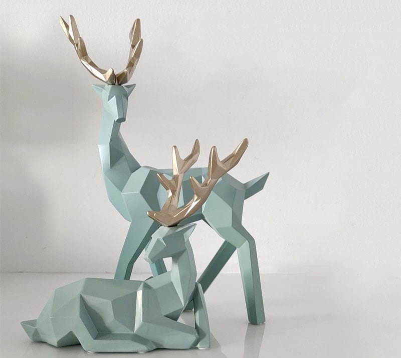 Two geometric deer sculptures in green, one standing and another sitting, displayed on a table.