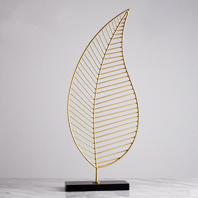 Elegant gold B-style leaf sculpture on sleek marble table.