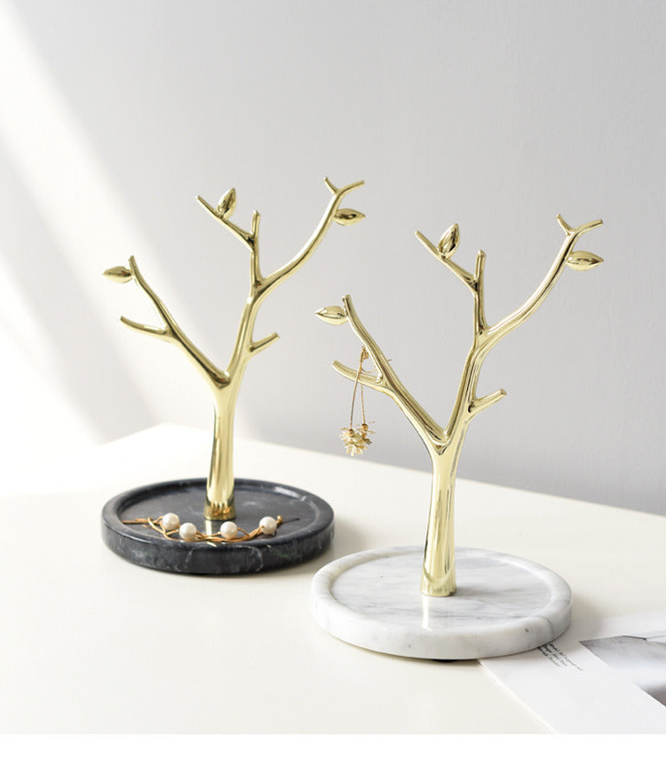 Jewels display on two gold metal tree-shaped jewelry stands towers, one with white marble base, another with black.