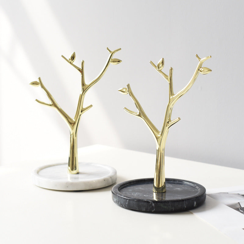 Display for two gold metal tree-shaped jewelry stands towers, one with white marble base, another with black.