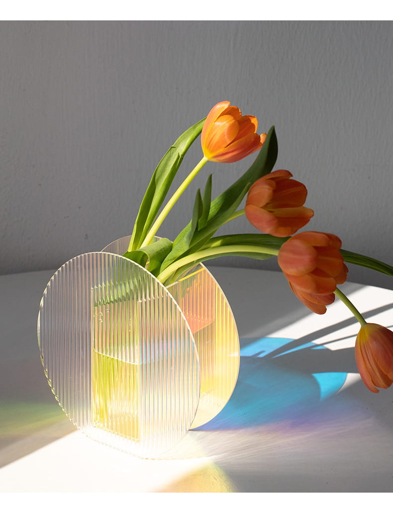 Round modern colorful acrylic vase is displayed on the table.