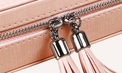 Close-up of pullers for pink portable jewelry box designed with tassels and zipper closure.