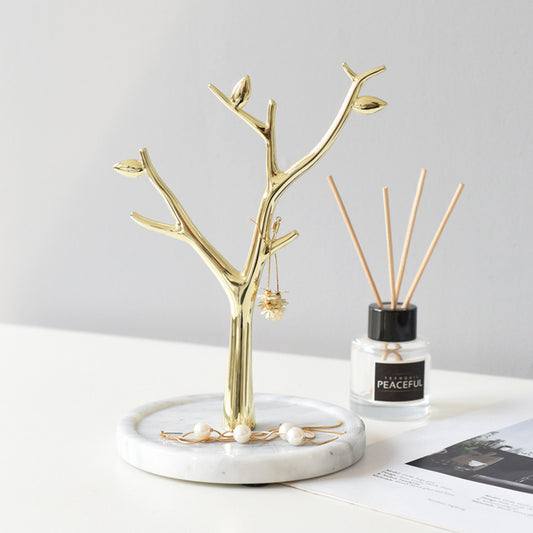 Jewels display on gold metal tree-shaped jewelry stand tower with white marble base.
