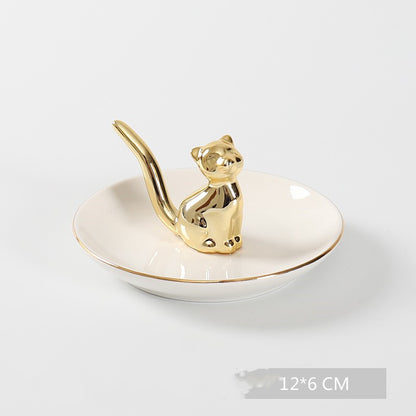 White ceramic jewelry tray with gold rim, and a golden cat sitting on the middle of the dish.