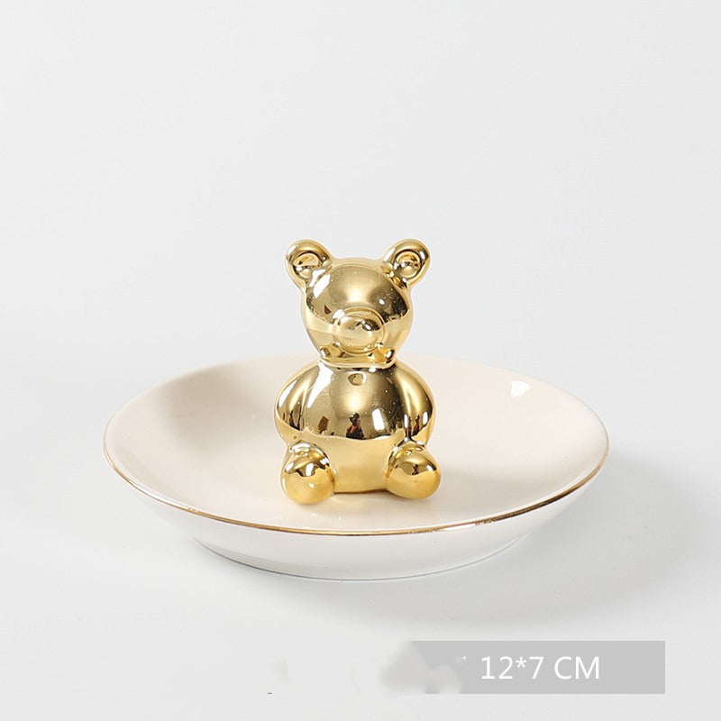 White ceramic jewelry tray with gold rim, and a golden bear sitting on the middle of the dish.