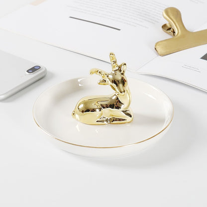 White ceramic jewelry tray with gold rim, and a golden deer sitting on the middle of the dish.