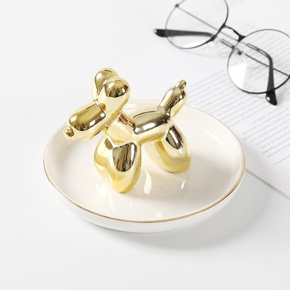 White ceramic jewelry tray with gold rim, and a golden dachshund standing on the middle of the dish.