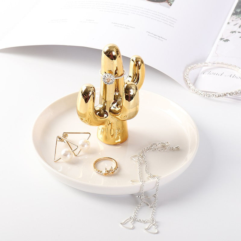 White ceramic jewelry tray with gold rim, and a golden cactus standing on the middle of the dish.