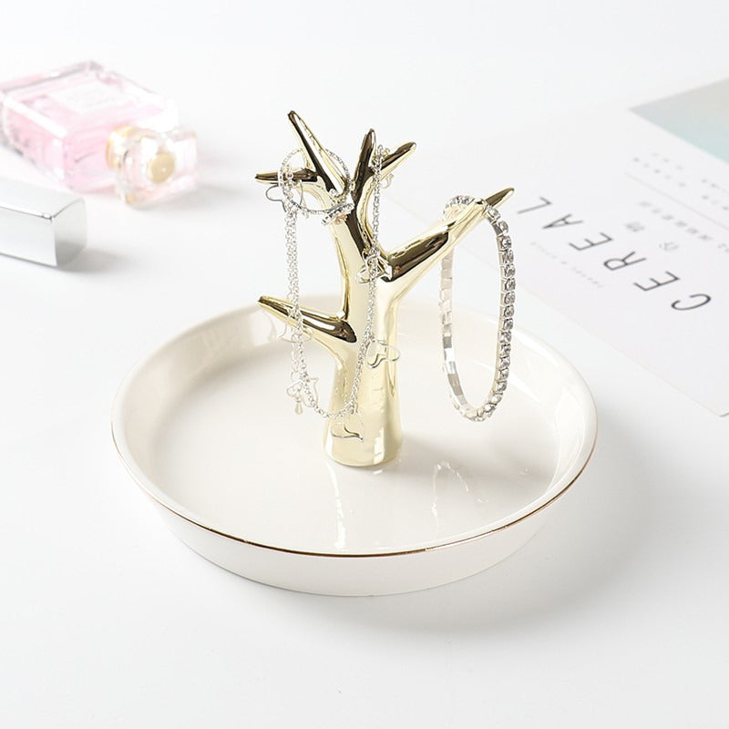 White ceramic jewelry tray with gold rim, and a golden tree standing on the middle of the dish.