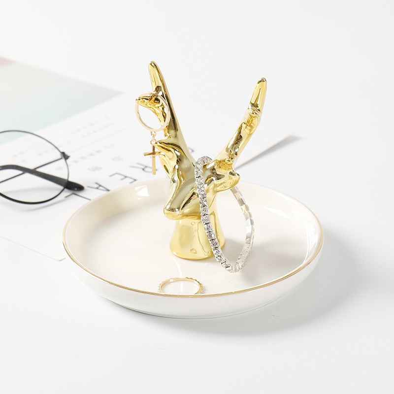 White ceramic jewelry tray with gold rim, and a golden antler standing on the middle of the dish.