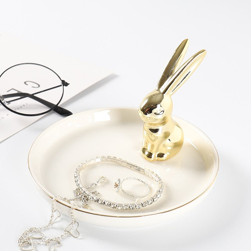 White ceramic jewelry tray with gold rim, and a golden rabbit sitting on the edge of the dish.