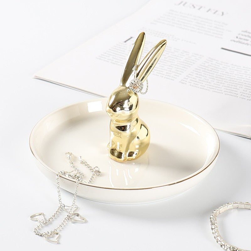 White ceramic jewelry tray with gold rim, and a golden rabbit sitting on the middle of the dish.